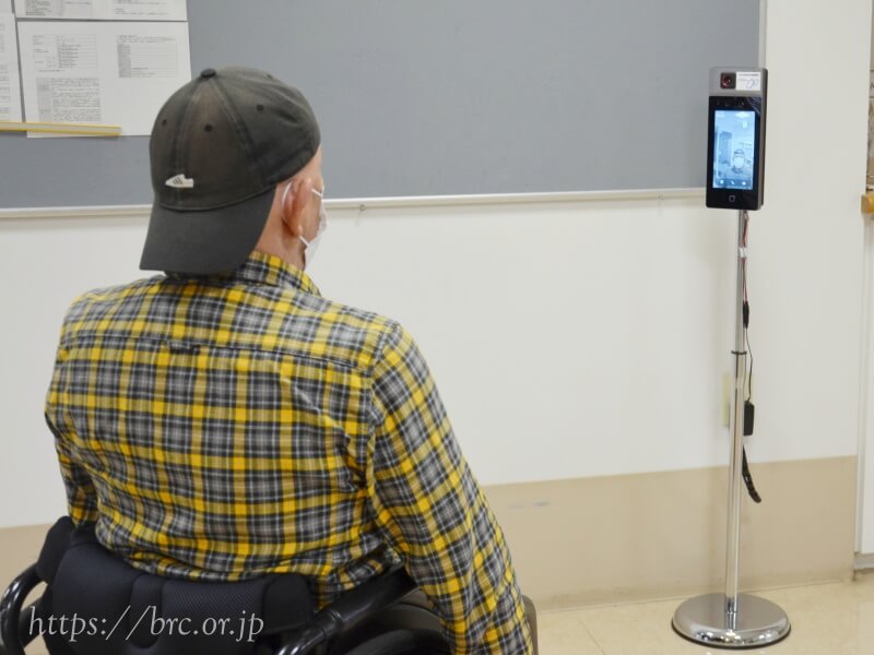 障害福祉サービス事業所みのりに設置されたサーマルカメラで体温測定する利用者の男性