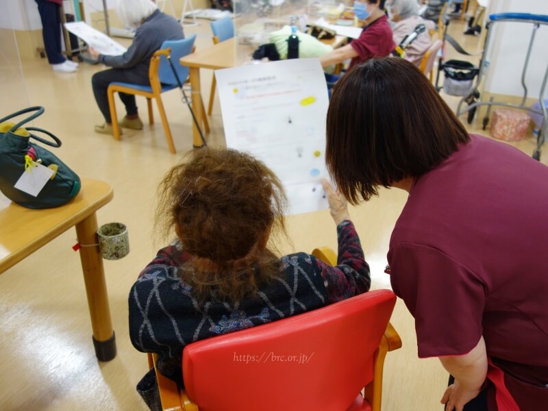 職員と講話の資料をご覧になる利用者さま